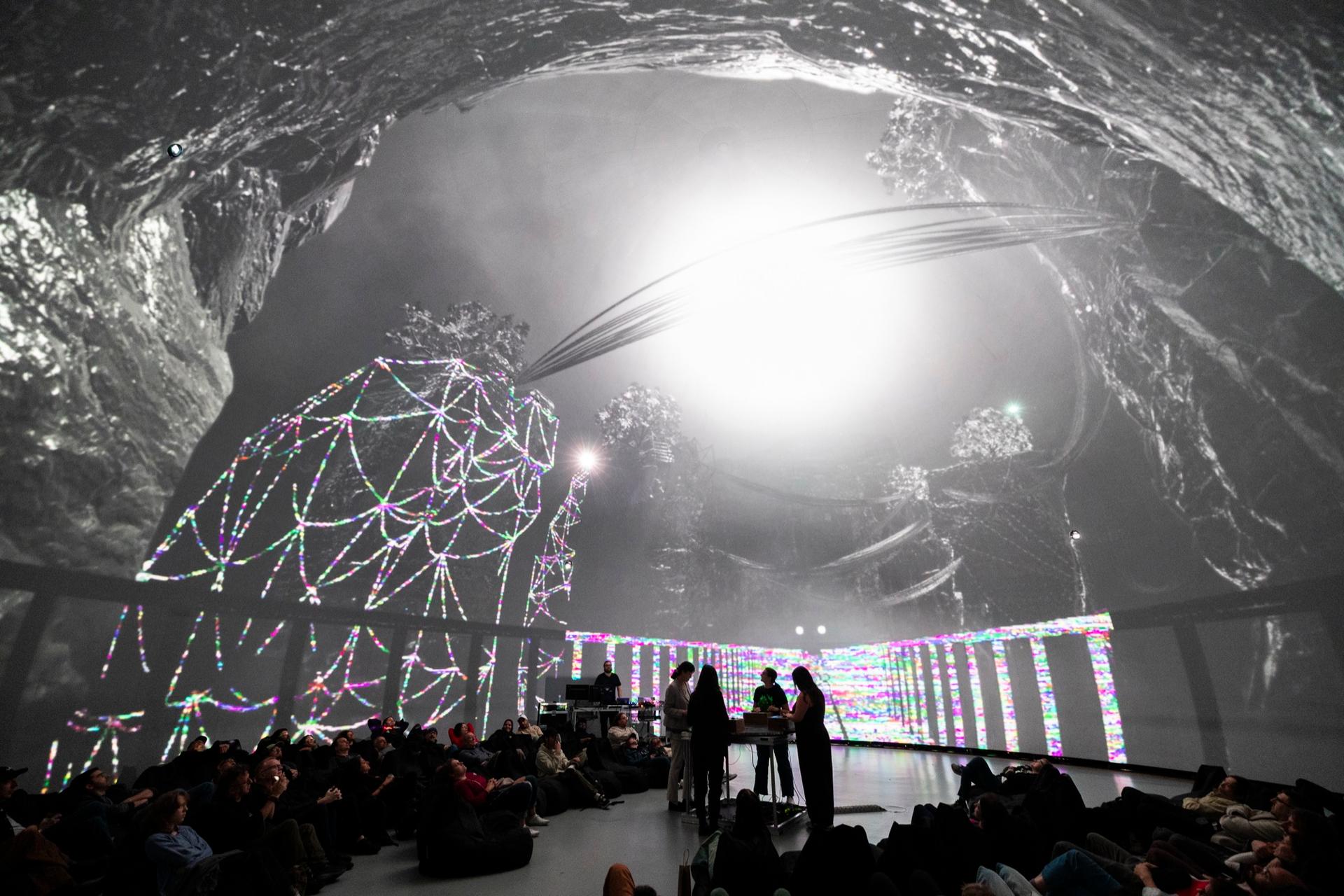 Performers at the centre of the dome under a projected cave and a glowing sphere