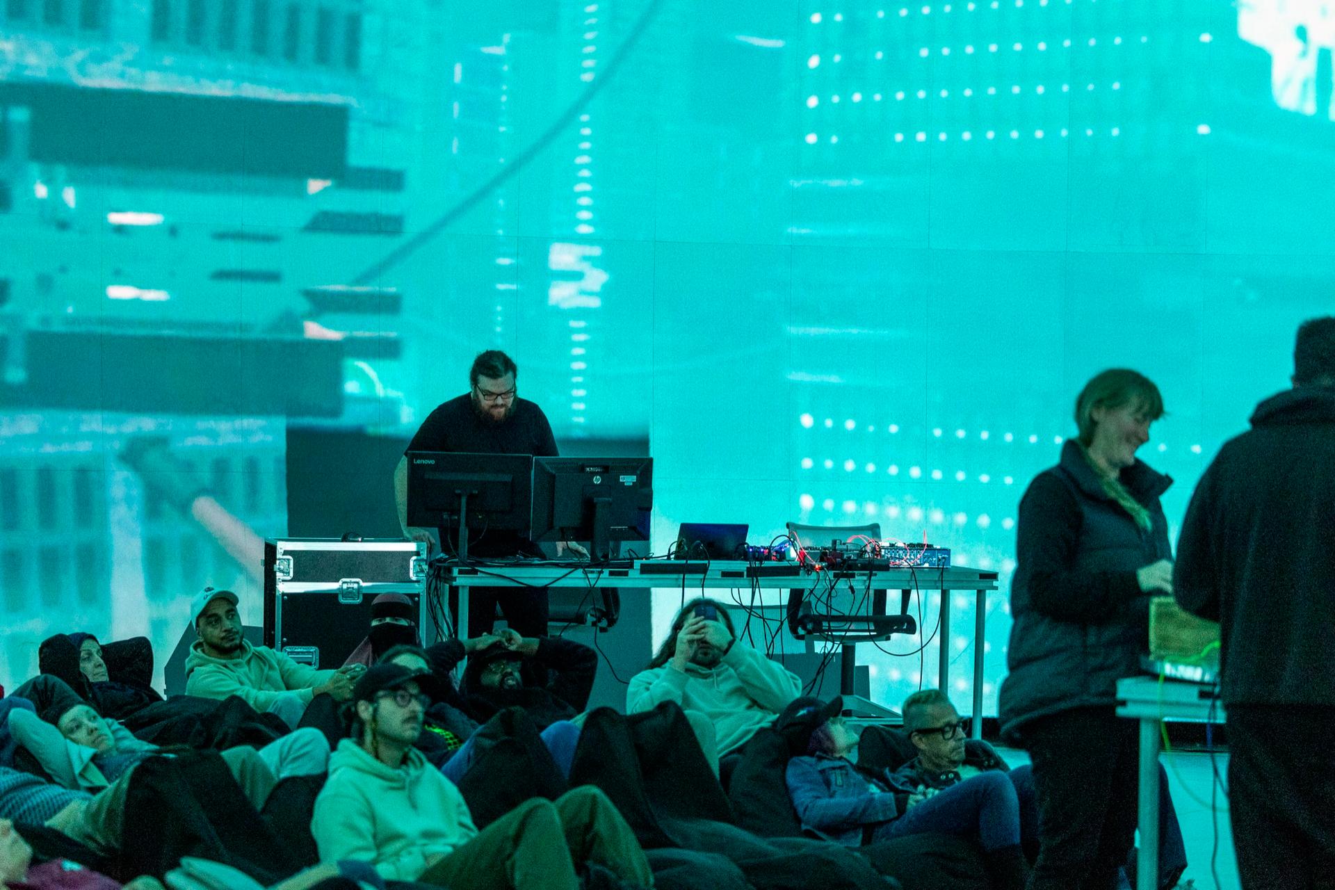 Audience on beanbags in front of the performance desk and a cyan cityscape